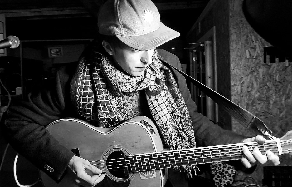 Reuben Lovett performing live on acoustic guitar, black and white photo