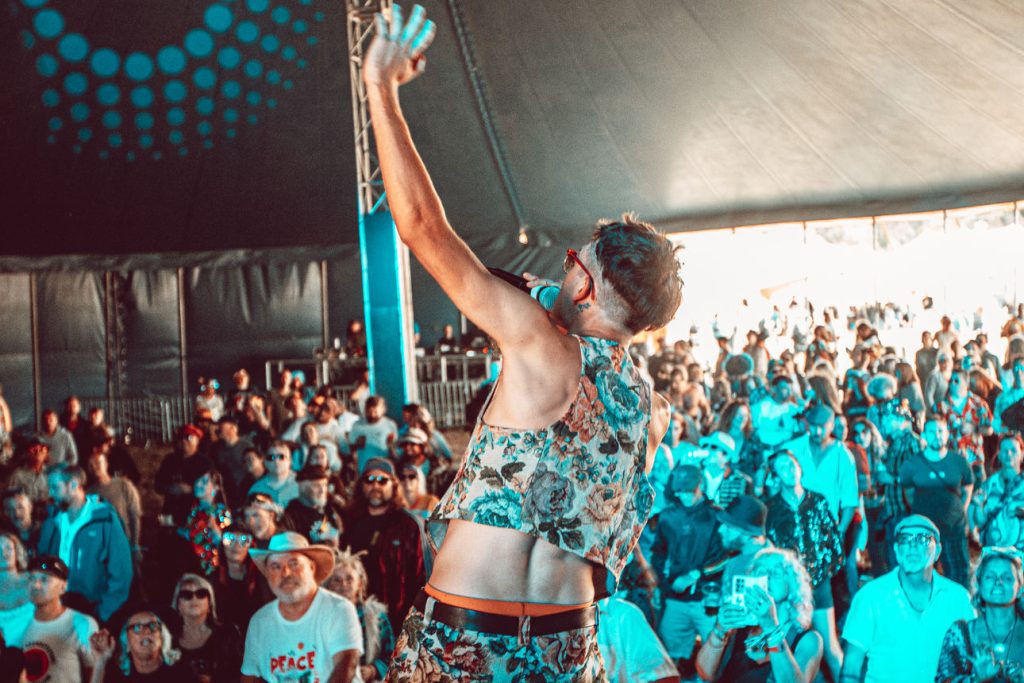 Down to the Nub, Chepstow Dub Catalyst performing live at Mucky Weekender 2026, Reuben singing to the crowd with one arm raised, seen from behind on stage.